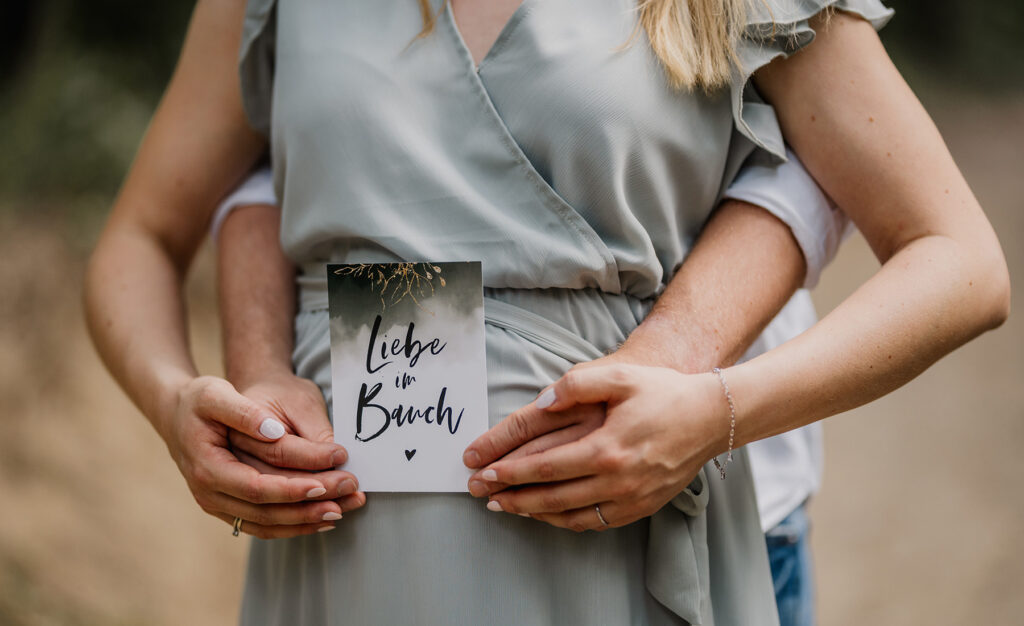 Werdende Eltern halten ein Schild Hallo Baby vor dem Babybauch – Sabrina Dötzl Fotografie Hollabrunn