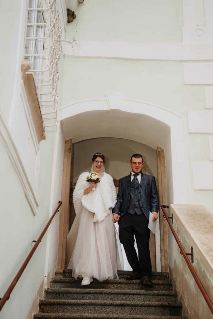 Brautpaar kommt eine Treppe aus einem weißen Torbogen herunter – Sabrina Dötzl Fotografie Hollabrunn
