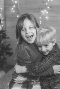 Geschwister umarmen sich lachend beim Weihnachtsshooting, helles Schwarz-Weiß-Foto – Sabrina Dötzl Fotografie Hollabrunn